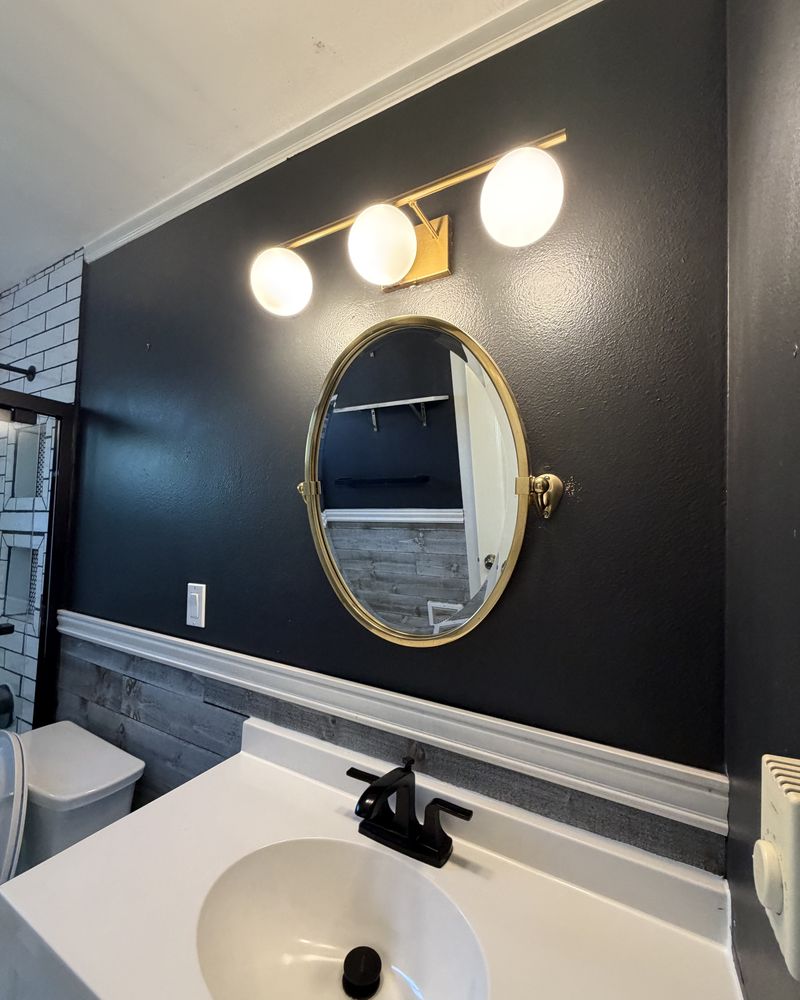 Clean bathroom with a navy wall, round gold mirror and white sink